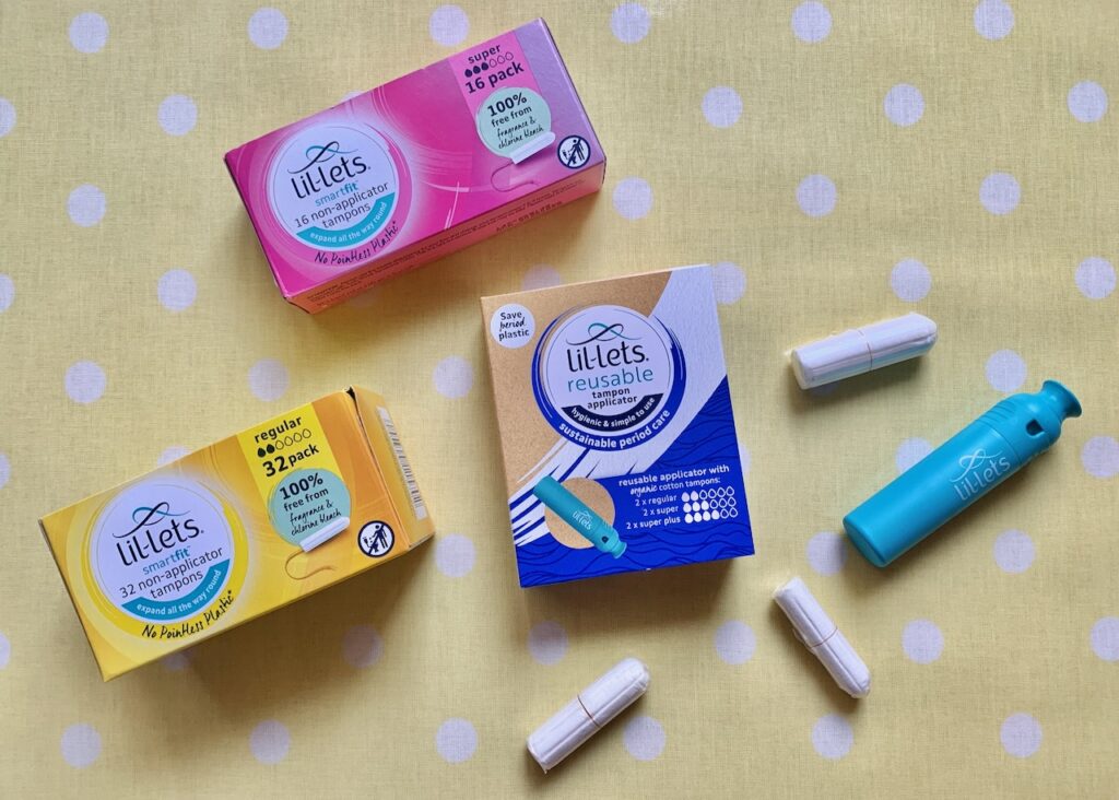 Three boxes of tampons on a table with loose tampons and a reusable applicator laid out.