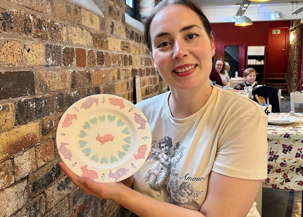 Becky holds up her finished decorated Emma Bridgewater plate with rabbits on it.