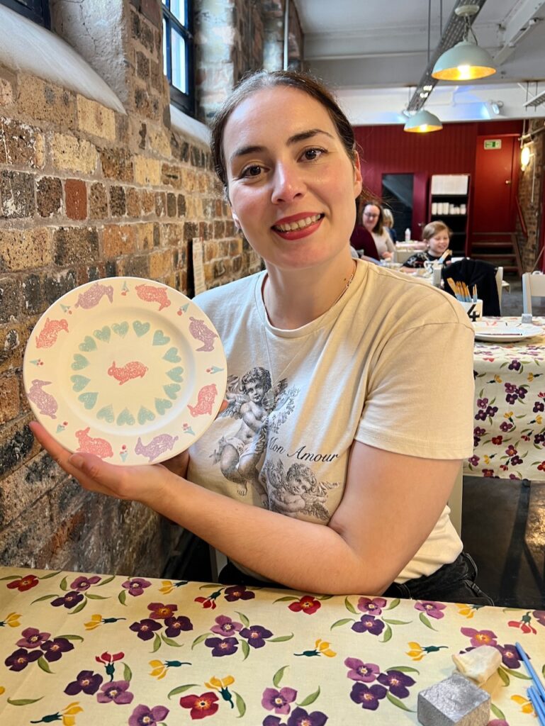 Becky shows off her finished decorated plate with sponge prints of rabbits.