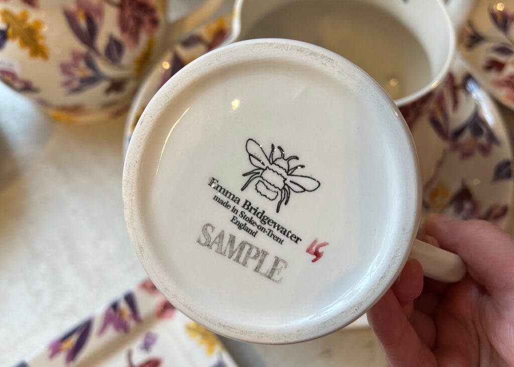 Becky holds up the bottom of a mug with sample printed on it.